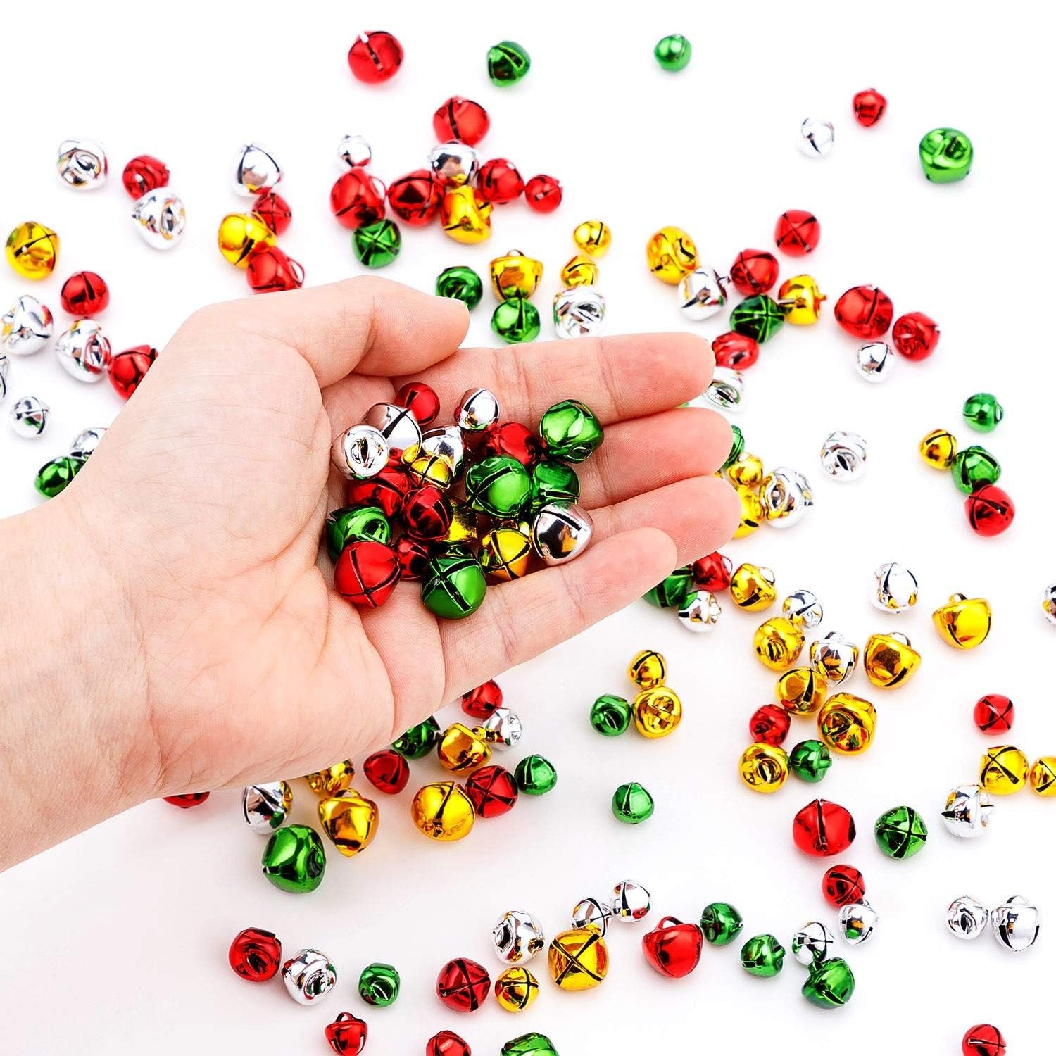 Hand holding colorful Christmas jingle bells in red, green, gold, and silver. Bells are scattered on a white background.