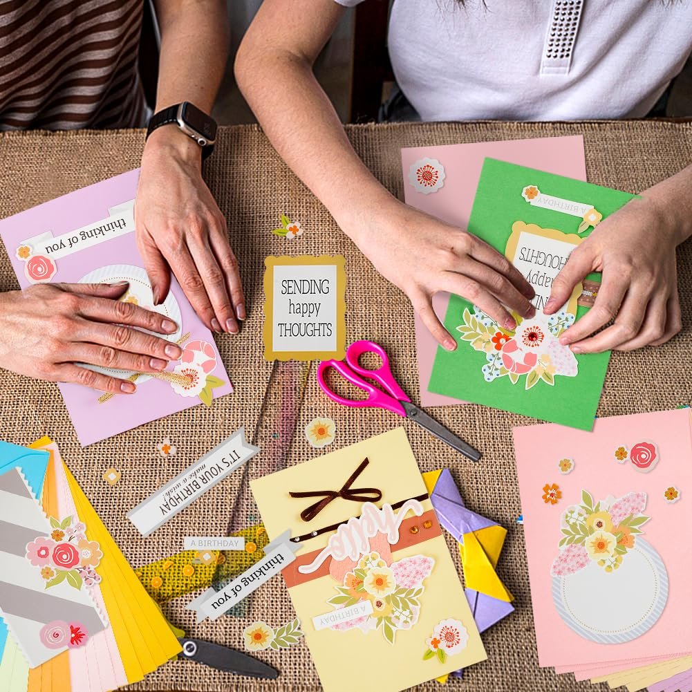 Hands crafting greeting cards with colorful paper, stickers, and scissors on a burlap surface.