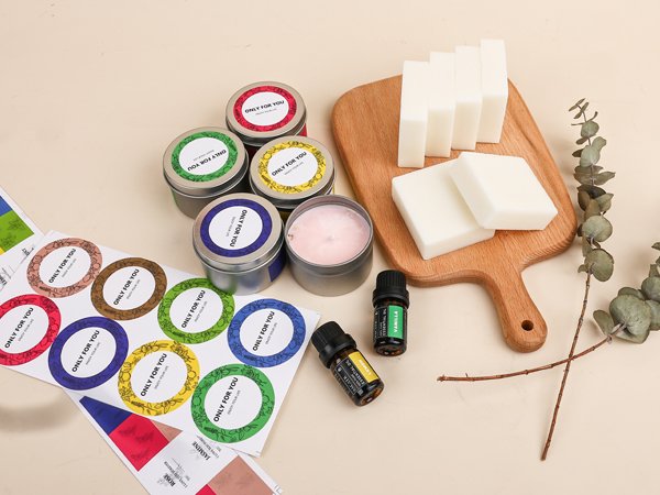 Soy candle making kit contents including wax blocks, tins, essential oil bottles, and decorative stickers on a light background.