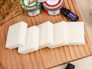 Soy wax blocks and essential oil bottles arranged on a wooden cutting board with dried greenery