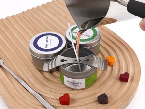 Soy candle making kit with wax pouring into a tin, surrounded by colorful wax melts and wicks.