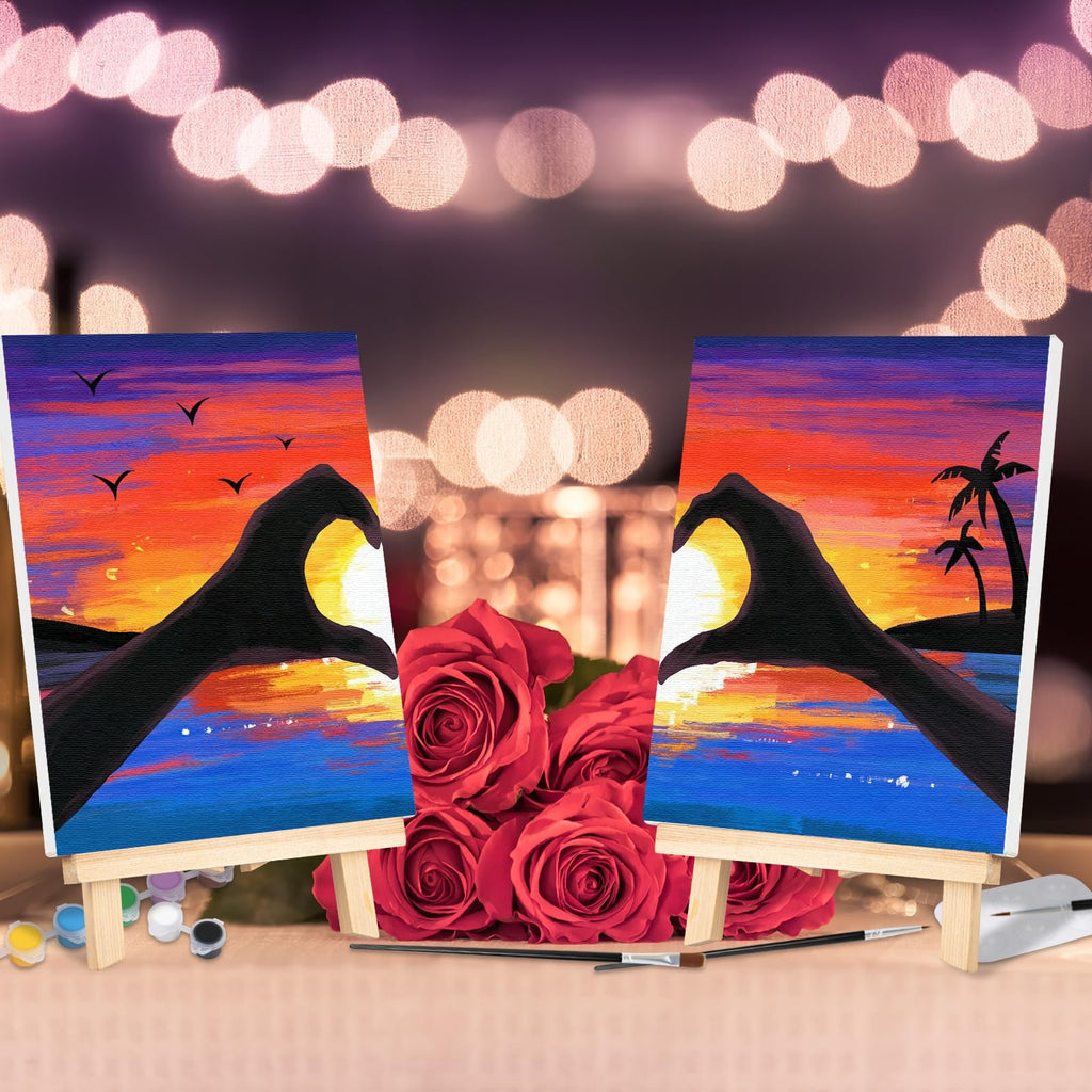 Two pre-drawn canvases showing a sunset with hands forming a heart, displayed on easels with roses and paint supplies.