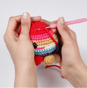Hands crocheting a colorful stuffed octopus toy with a pink crochet hook and red yarn.