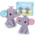 Two crocheted elephants, one with blue accents and one with pink accents, sit in front of a product box with a cartoon sun and clouds.