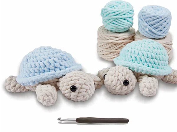 Two crocheted turtles with blue shells and yarn balls and crochet hook on white background
