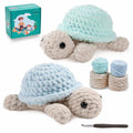 Two plush crochet turtles, one light blue and one teal, with yarn balls and a crochet hook on a white background.