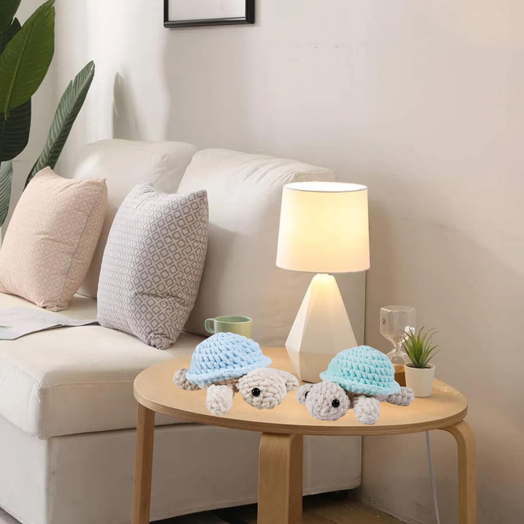 Two crocheted turtle toys with blue shells and light gray bodies on a wooden table next to a lamp and sofa.
