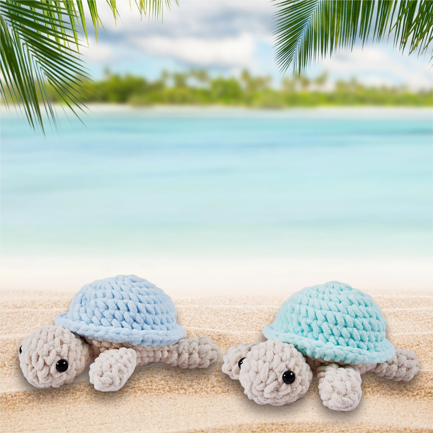 Two crocheted turtle toys with blue and teal shells on a sandy beach with palm fronds and ocean background.