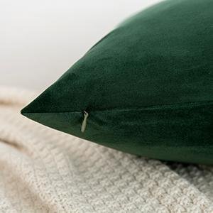Close-up of a dark green velvet throw pillow cover showing a zipper detail on a cream textured blanket.