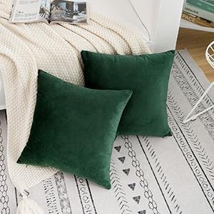 Two dark green velvet throw pillow covers on a rug next to a couch.
