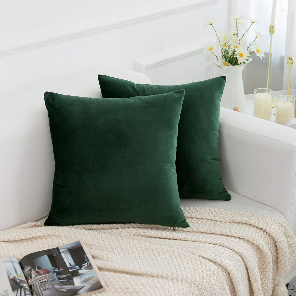 Two dark green velvet throw pillow covers on a white couch with a cream blanket and a magazine.