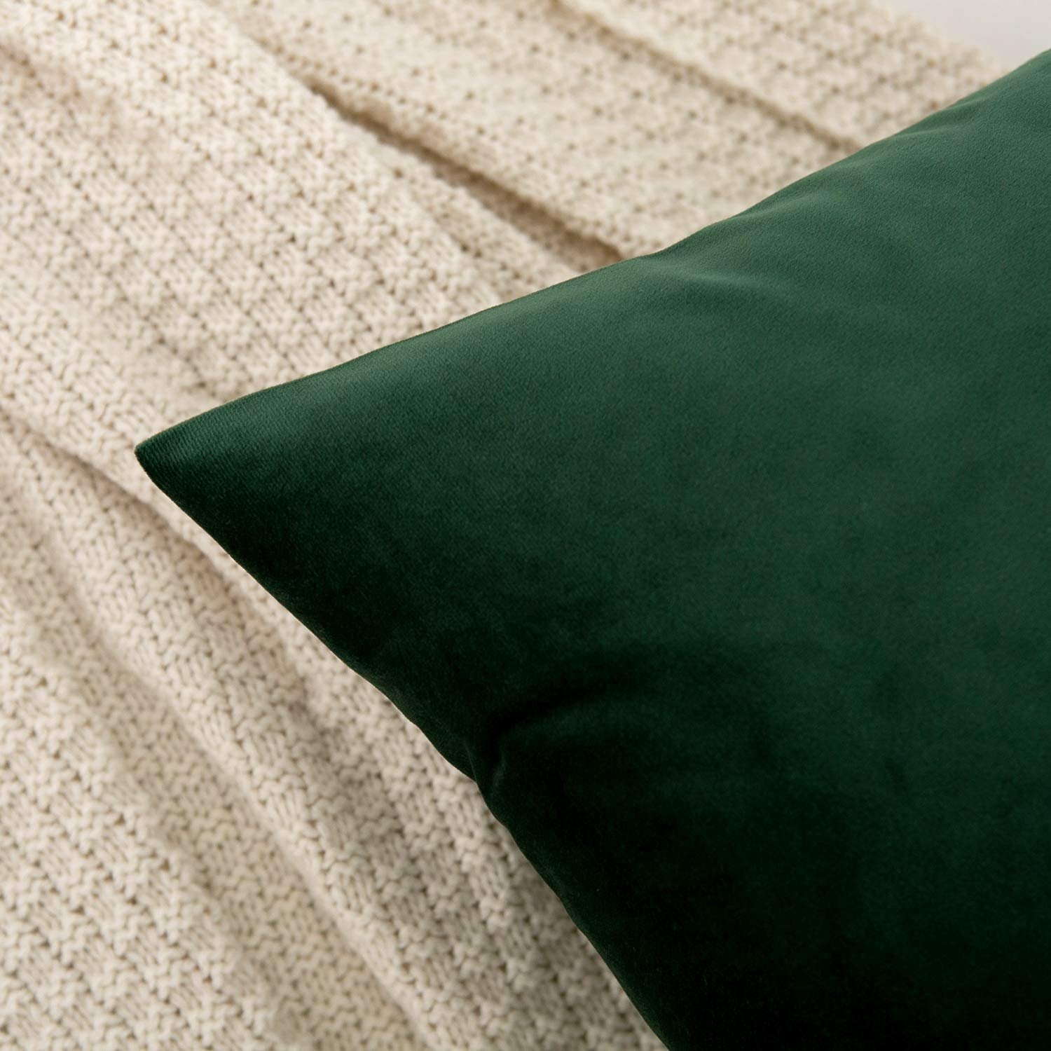 Dark green velvet throw pillow cover resting on a cream knit blanket, close-up shot.