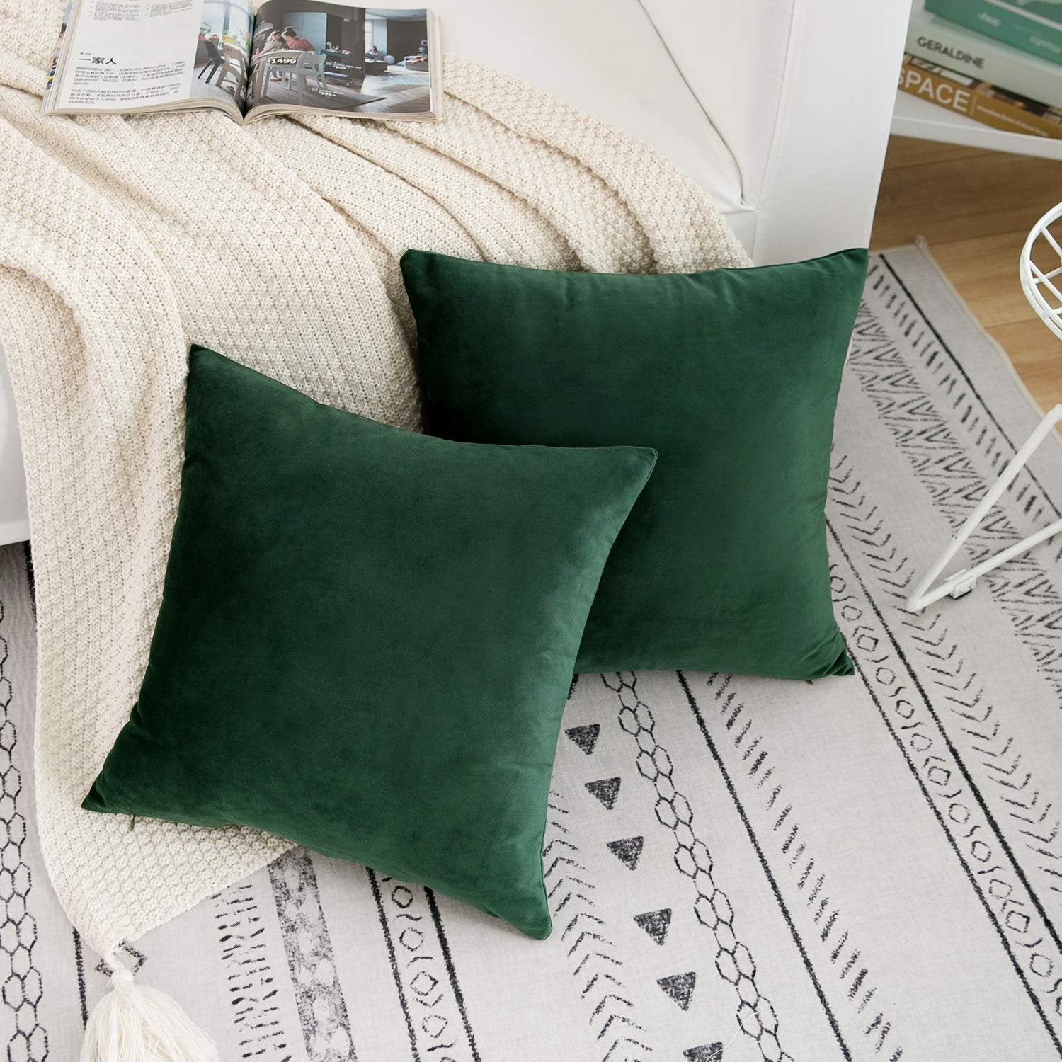 Two dark green velvet throw pillow covers on a cream knit blanket and patterned rug.