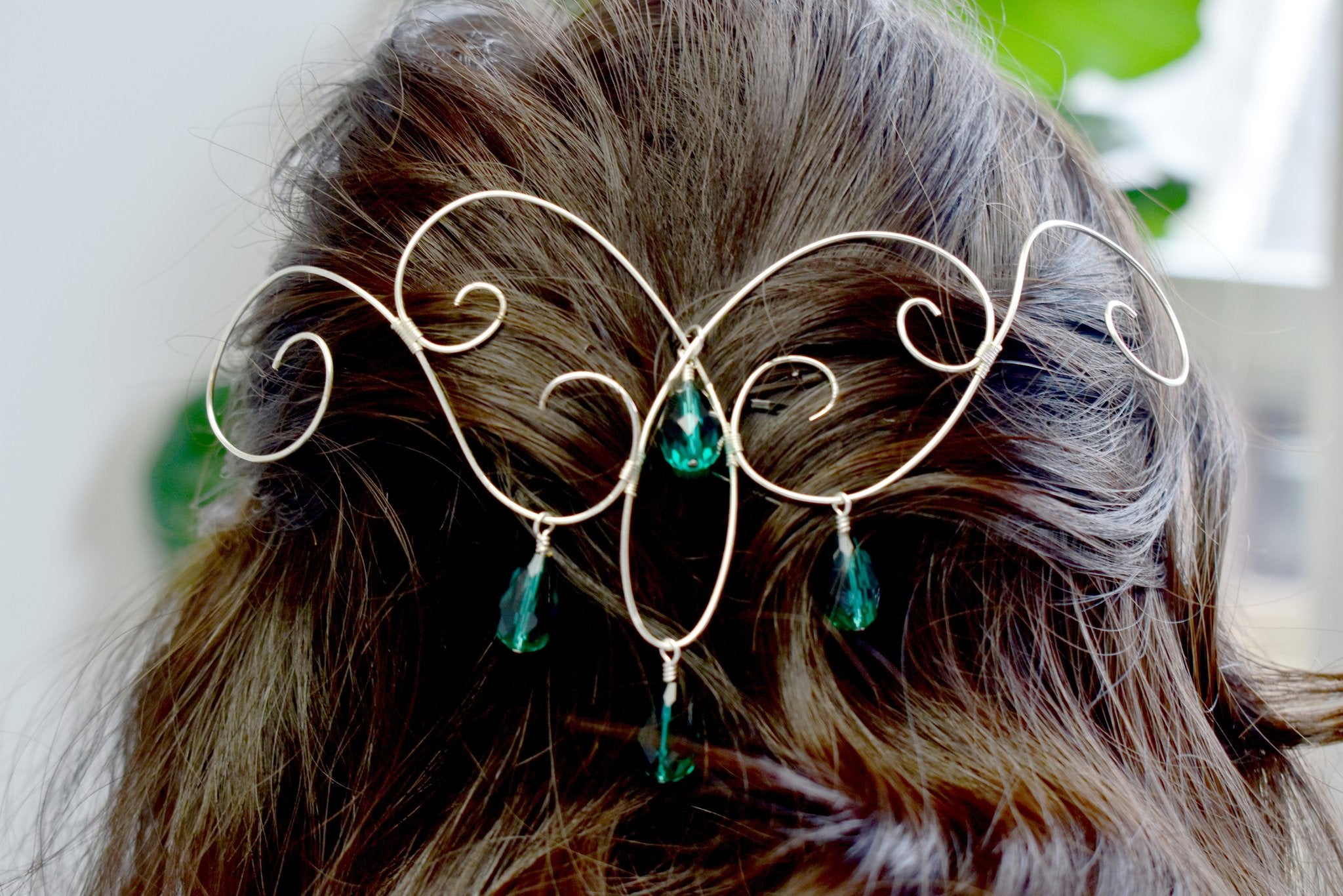 Close-up of a silver wire hair accessory with green teardrop beads, worn in dark hair.