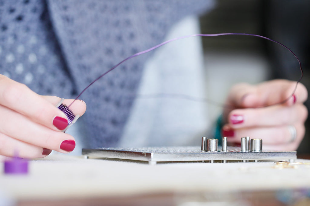 Close-up of hands using a wire jig for jewelry making, wrapping purple wire around a peg.