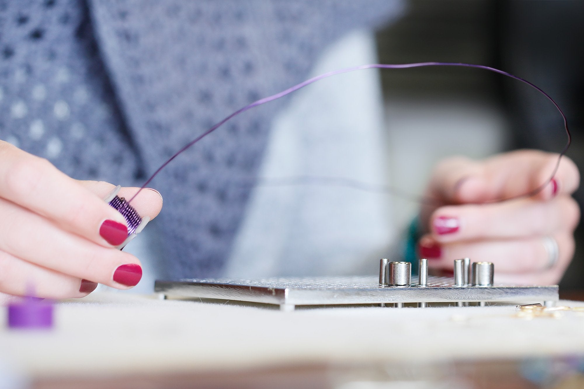 Close-up of hands using a wire jig for jewelry making, wrapping purple wire around a peg.