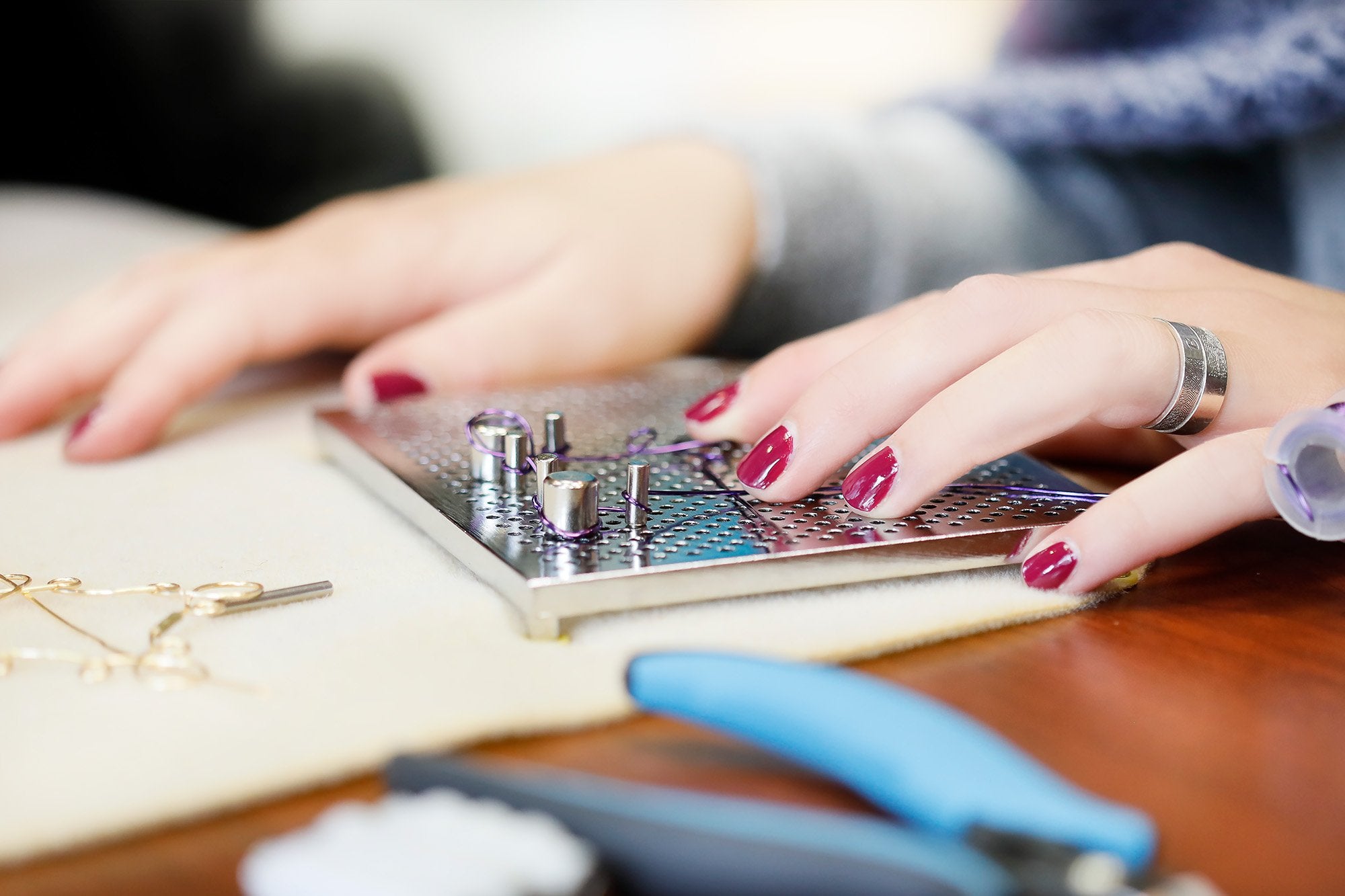 Hands using a wire jig board with pegs and purple wire for jewelry making