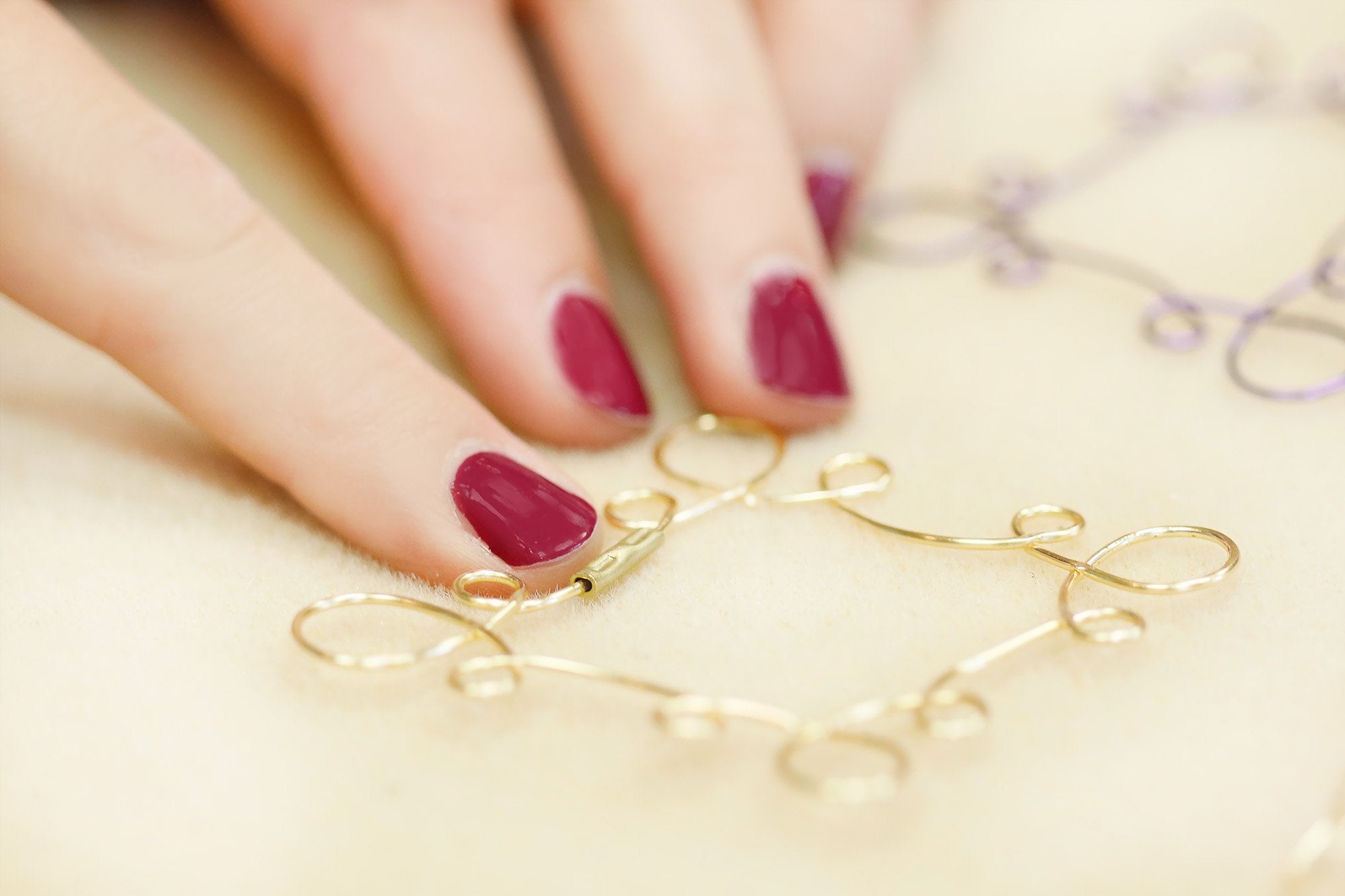 Close-up of hands creating wire art with gold and purple wire on a light beige surface.