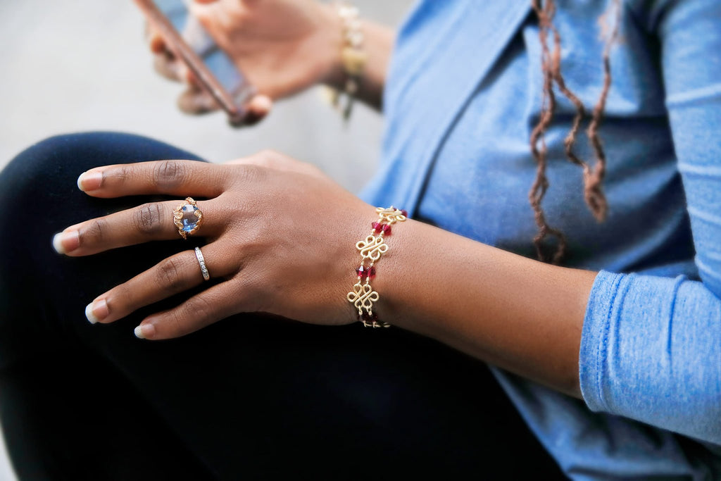 Close-up of a woman's hands wearing a large blue gemstone ring and a delicate bracelet, holding a smartphone.