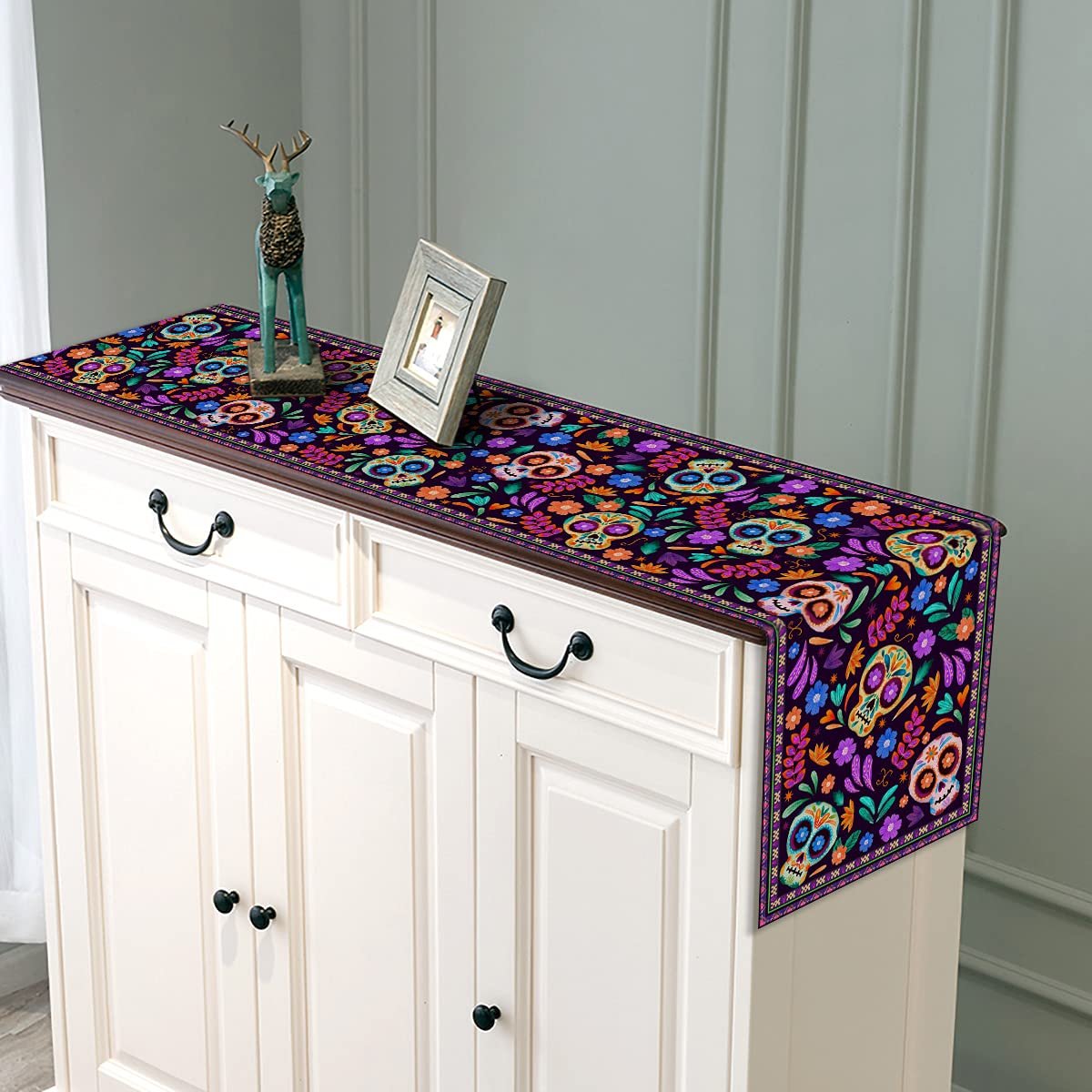 Dia De Los Muertos table runner with Mexican sugar skull and floral design draped over a white cabinet.