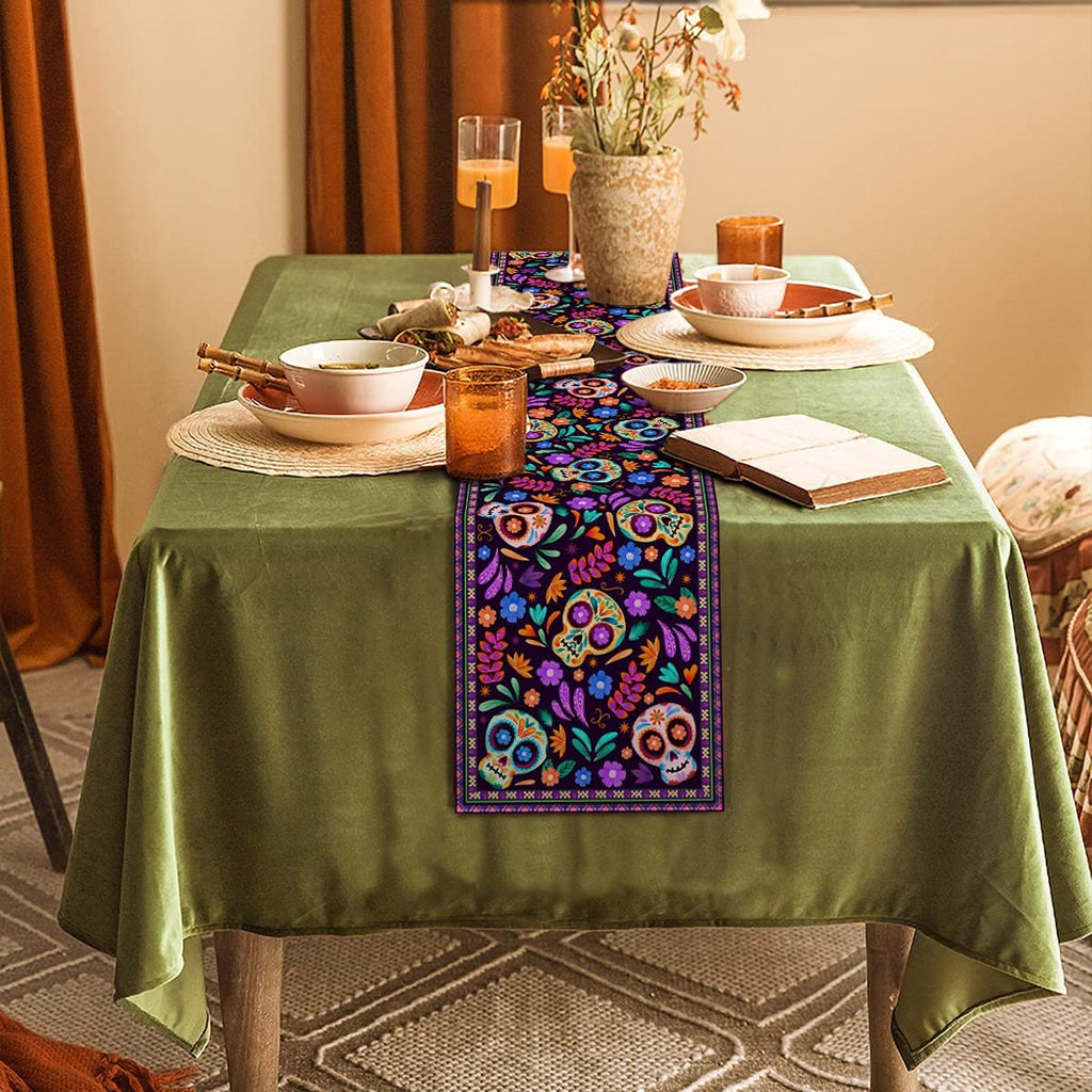 Dia De Los Muertos table runner with sugar skull design laid on a green tablecloth.