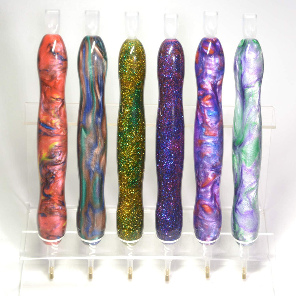 Six diamond painting drill pens with colorful swirled and glitter finishes displayed on a clear stand.