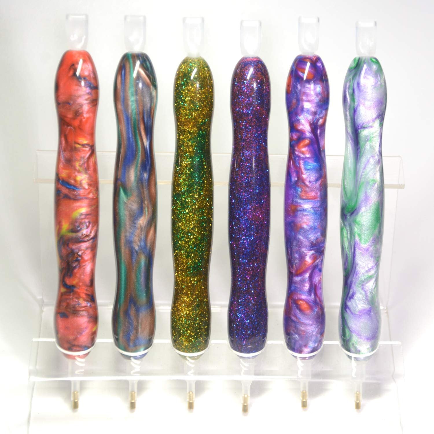 Six diamond painting drill pens with colorful swirled and glitter finishes displayed on a clear stand.