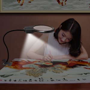 Diamond painting magnifier lamp with LED light clipped to a table where a woman is working on a painting.