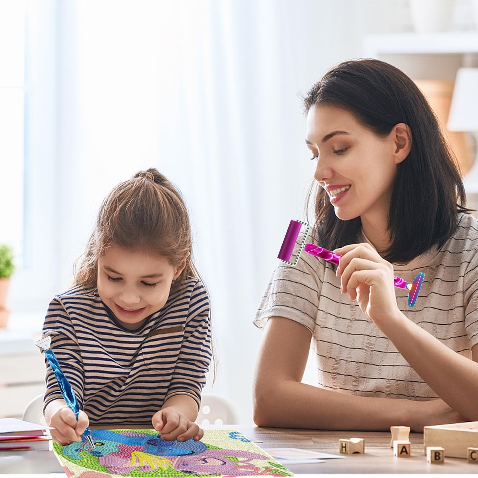 Mother and daughter doing diamond painting at a table, holding tools and smiling.