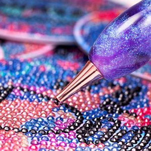 Diamond painting pen with rose gold tip applying a blue diamond to a colorful canvas
