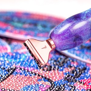 Diamond painting pen with rose gold tip on a colorful beaded canvas, close-up detail