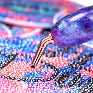 Close-up of a galaxy purple rose gold diamond painting pen with a stainless steel tip resting on a colorful diamond art canvas.