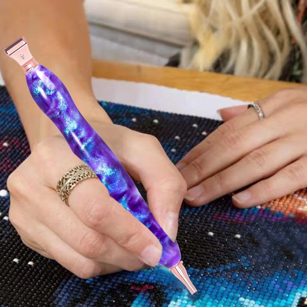 Diamond painting pen with galaxy purple and blue swirls being used to place a bead on a canvas.