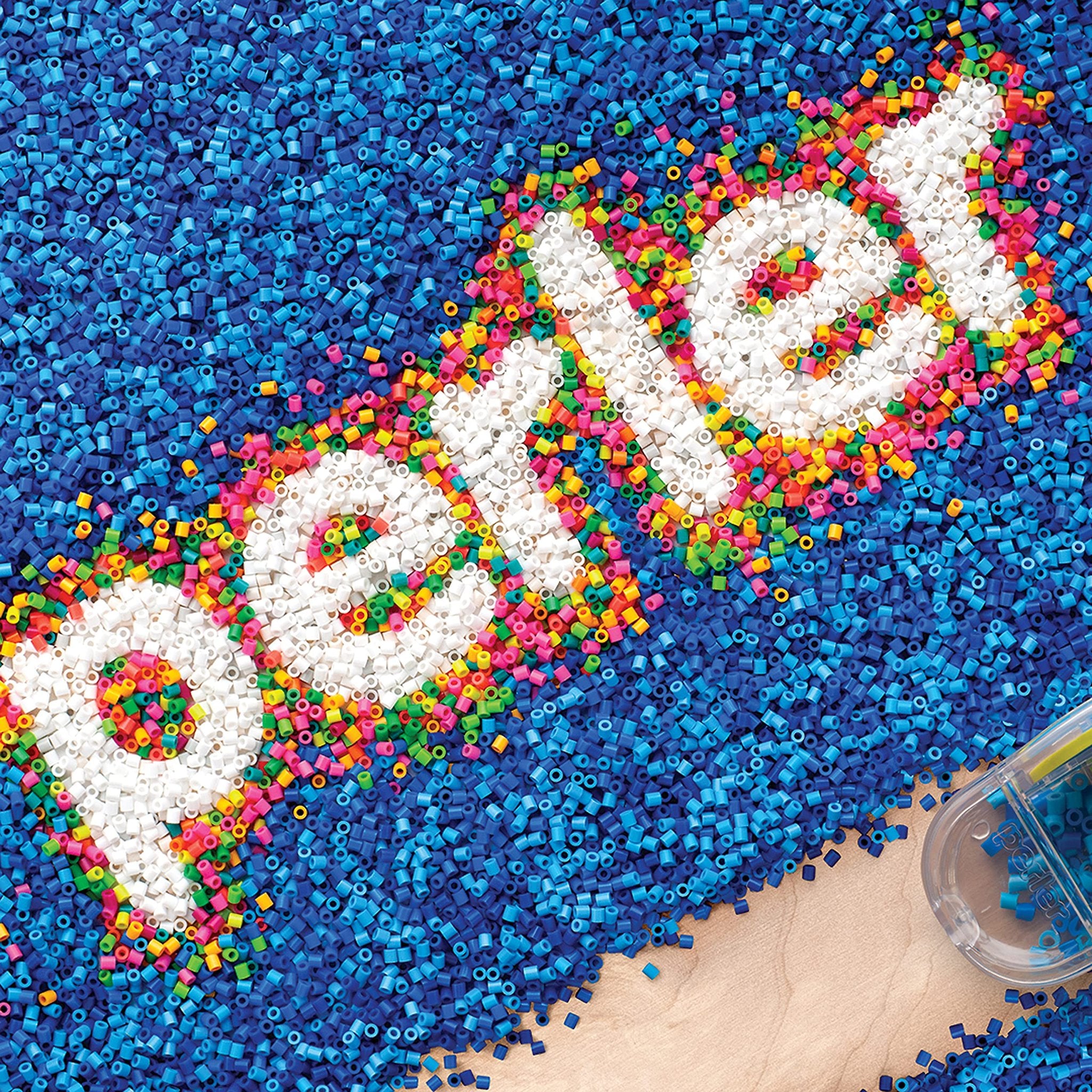 Fuse beads spelling out '' in white, surrounded by blue beads, with a clear bead container in the corner.