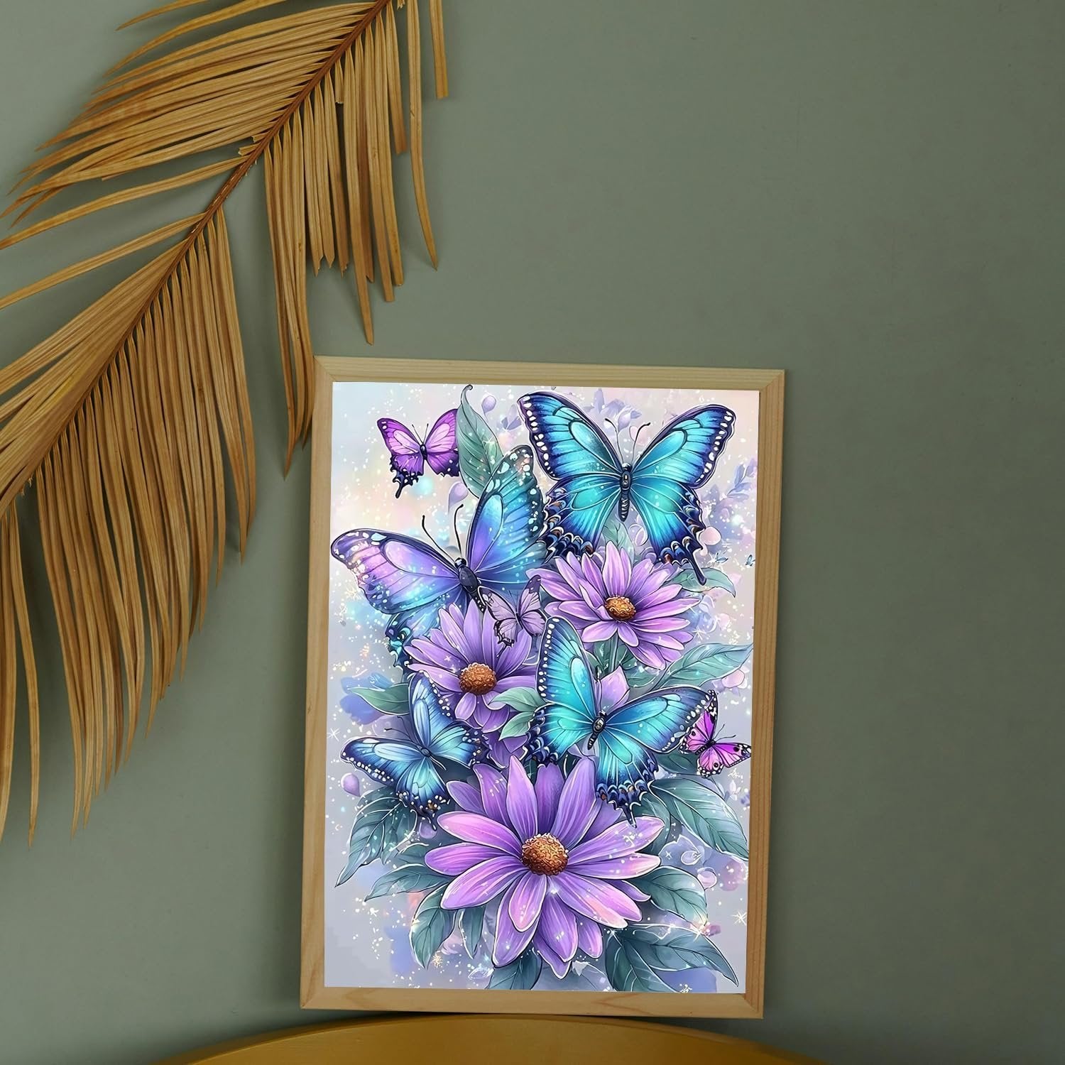 Framed diamond art kit featuring blue and purple butterflies on purple flowers, with a dried palm frond to the left.