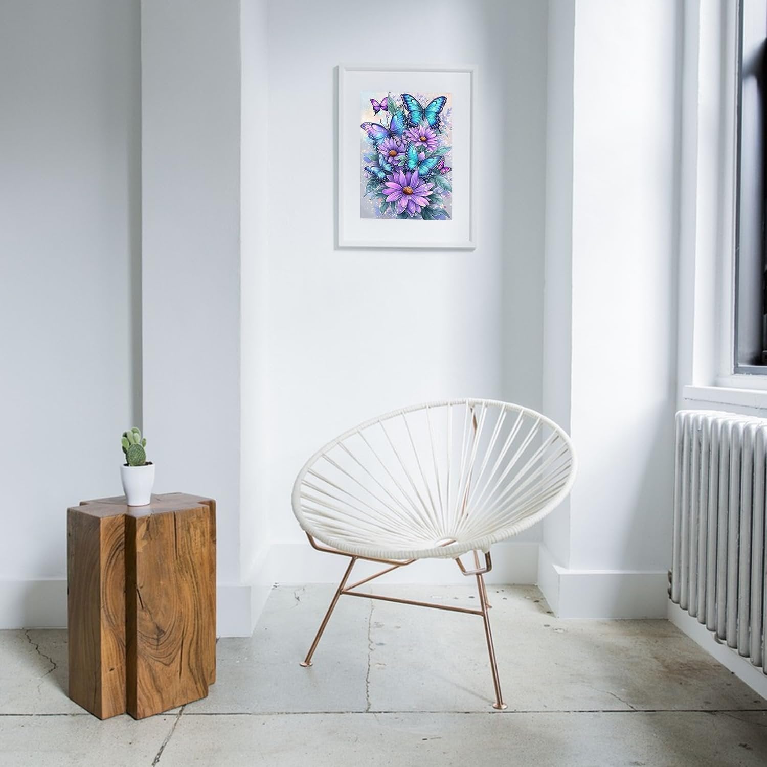 Framed butterfly and floral diamond art kit displayed on a white wall above a modern chair and wooden side table.