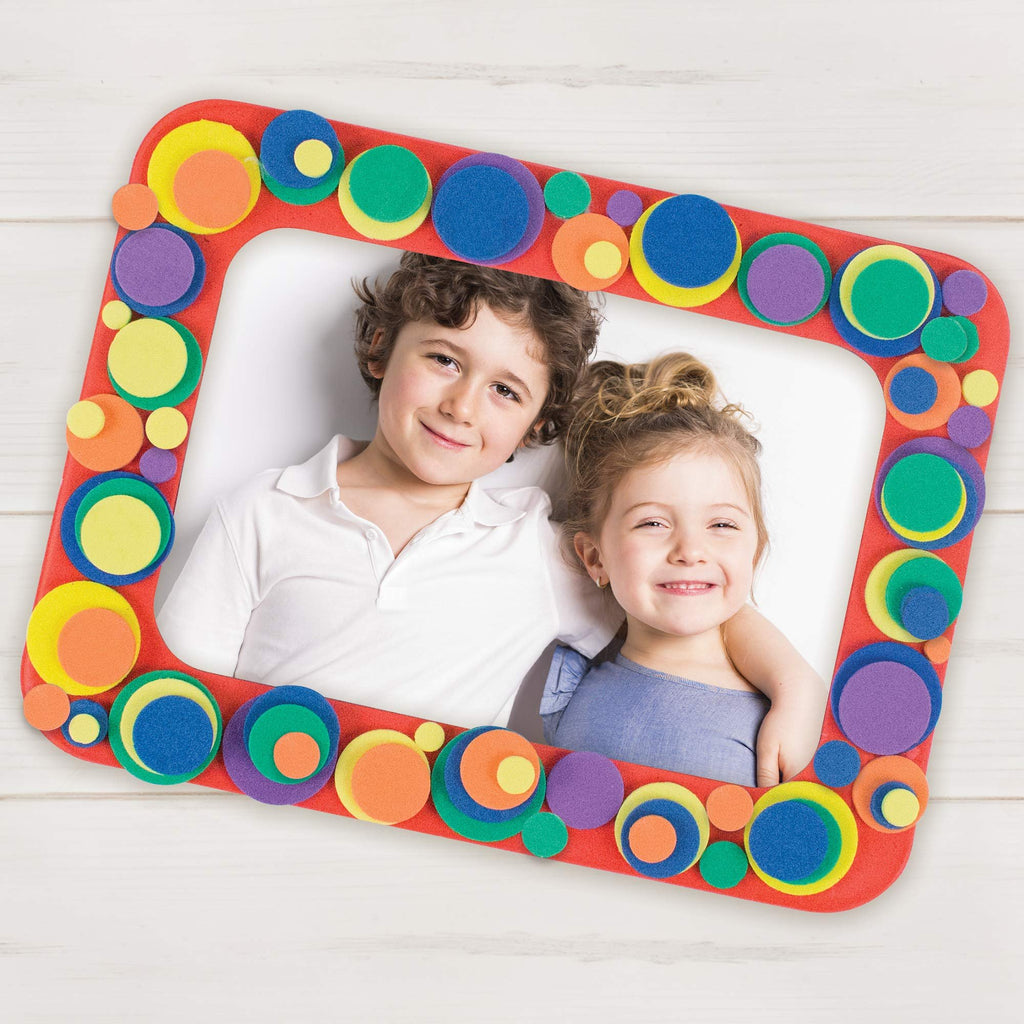 Children smiling behind a red foam picture frame decorated with colorful circles