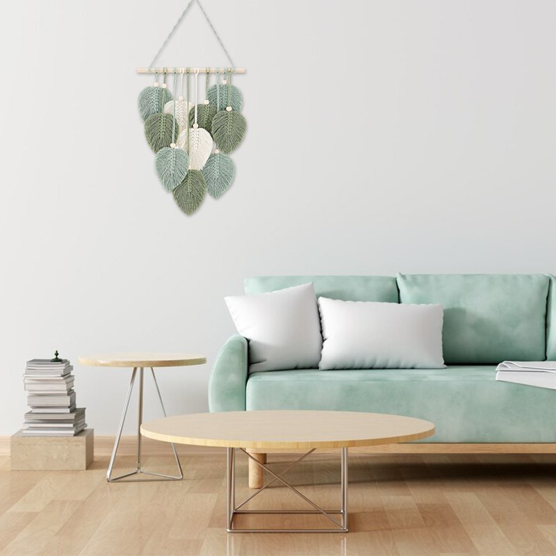 Macrame leaf wall hanging with wooden beads and stick, displayed above a sofa.