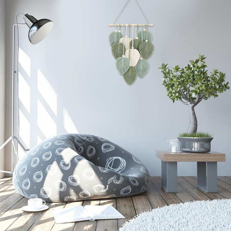 Macrame leaf wall hanging with wooden beads and stick, displayed in a modern living room setting.