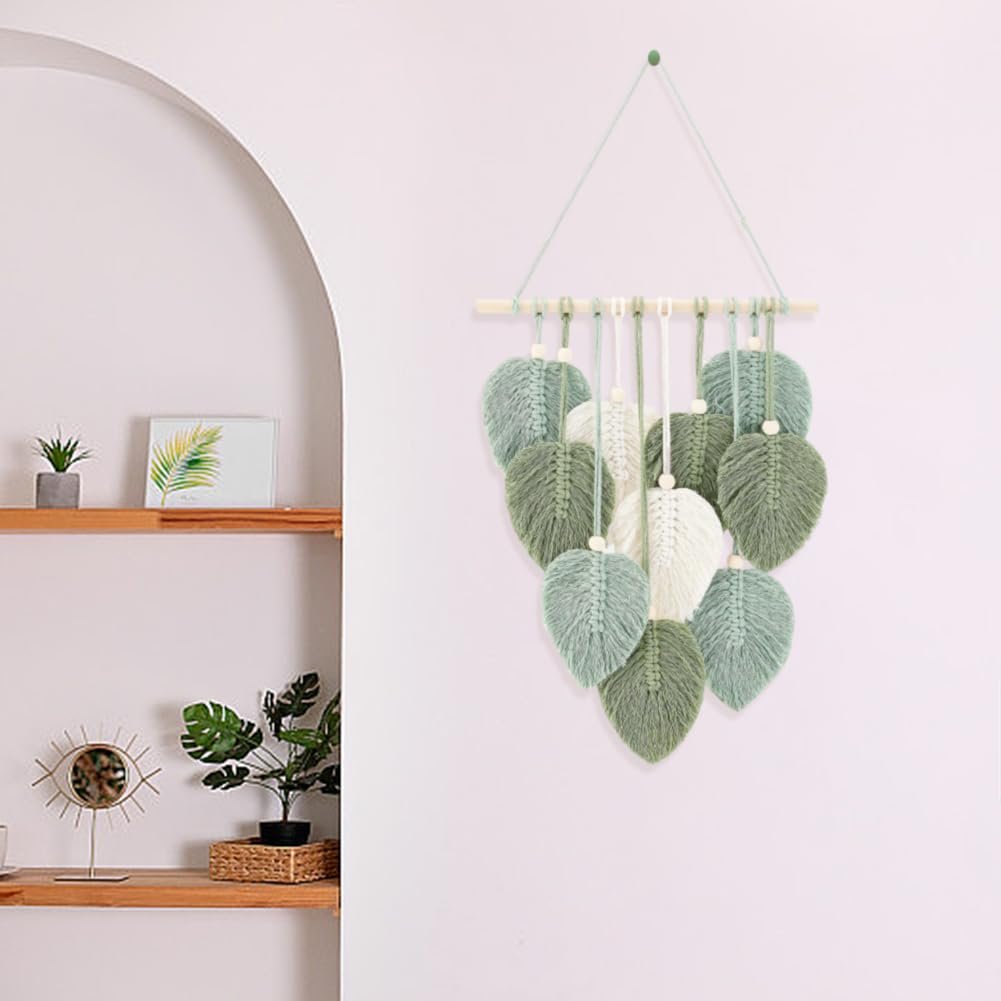 Macrame leaf wall hanging with wooden beads and stick, displayed on a wall with shelves and plants.