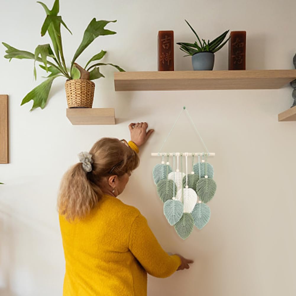 Woman hanging a macrame leaf wall hanging with green and white leaves on a wall