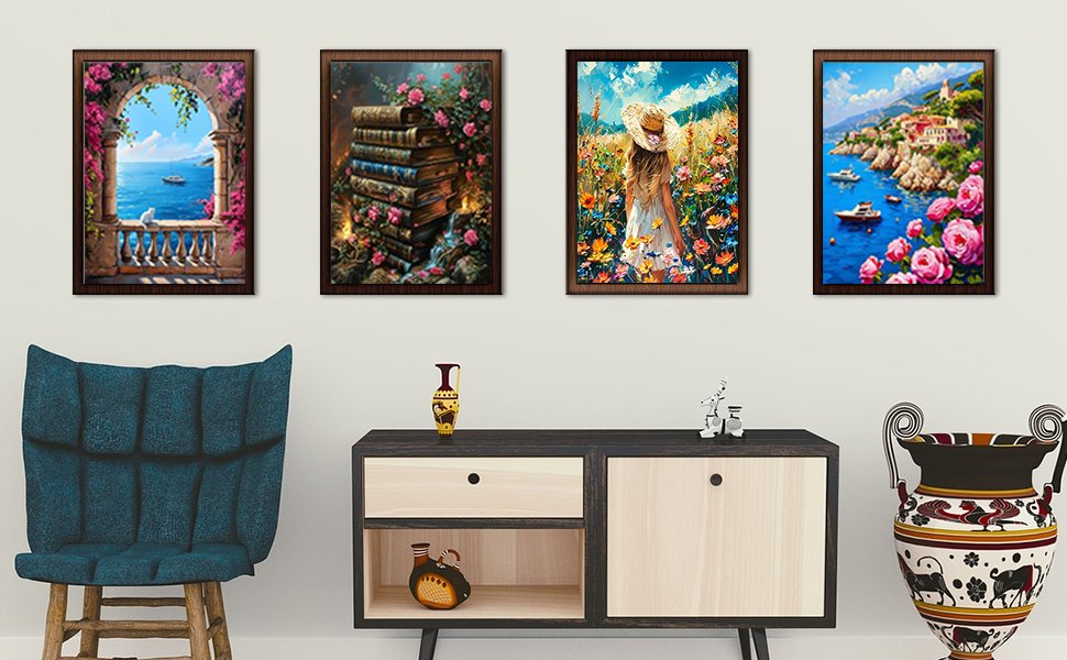 Four framed paint by numbers art pieces displayed on a wall above a cabinet, featuring a balcony scene, stacked books, a woman in a field, and a coastal village.