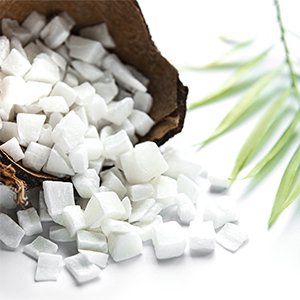 Coconut chunks spilling from a halved coconut shell with a green leaf sprig on a white background
