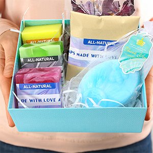 Hands holding a DIY soap making kit gift box with soap bars, shea butter, dried flowers, and essential oils.
