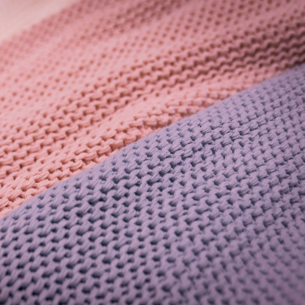 Close-up of knitted fabric in pink and purple hues, showing texture and stitch detail.