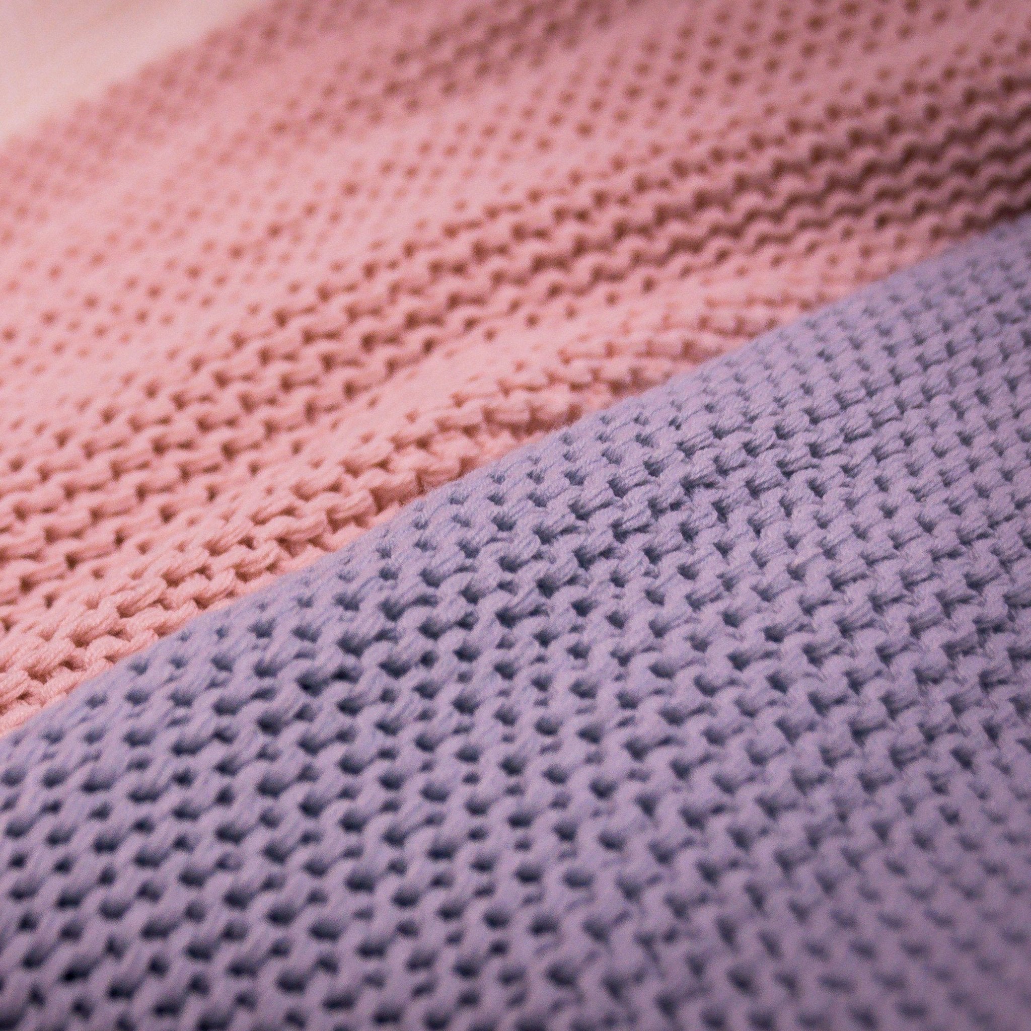 Close-up of knitted fabric in pink and purple hues, showing texture and stitch detail.