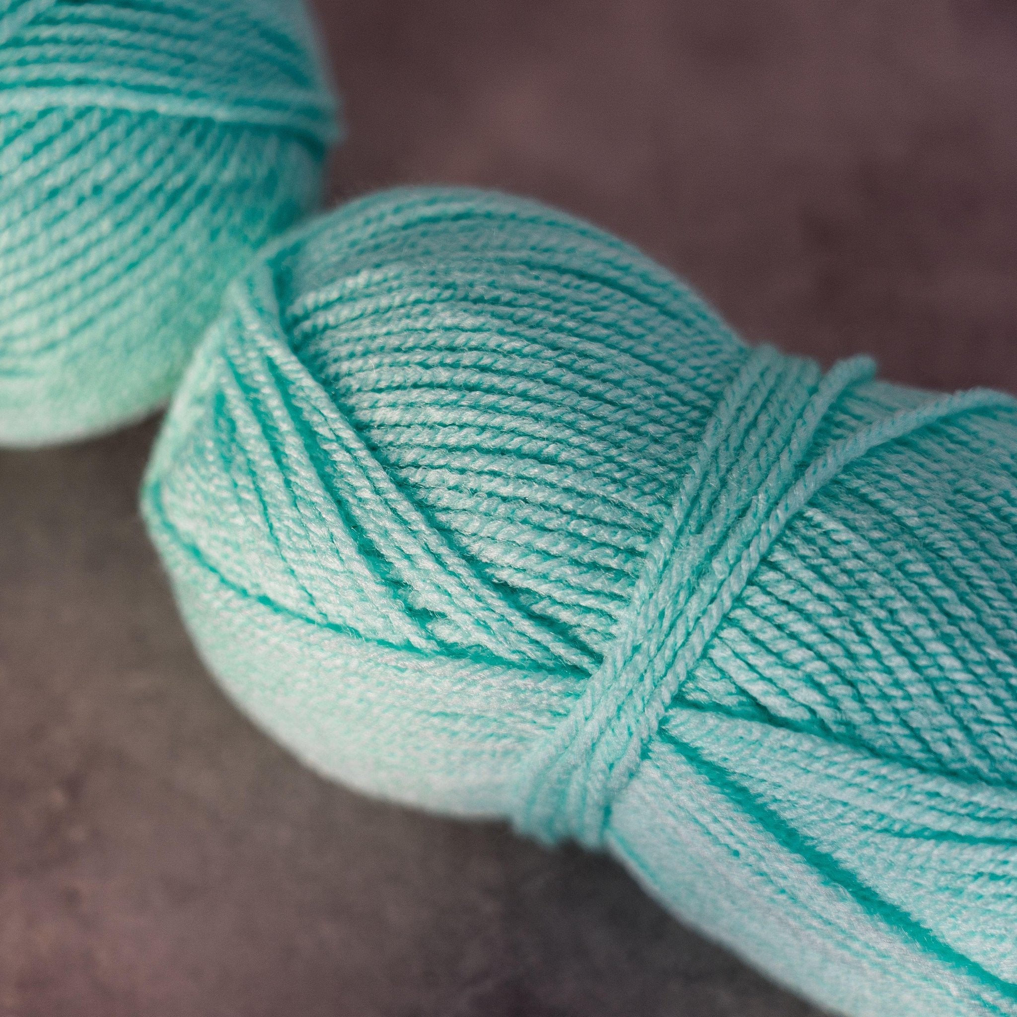 Close-up of two teal yarn skeins on a dark textured surface, one in focus.