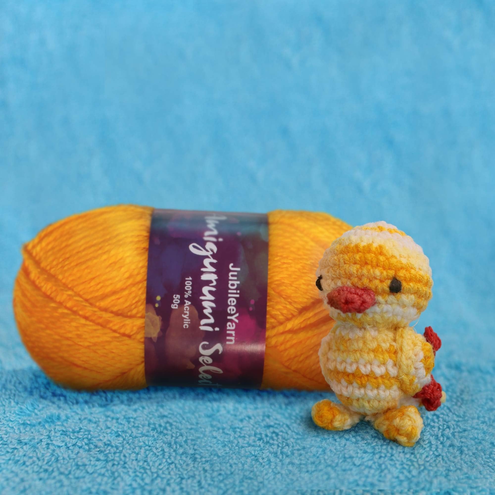 Orange acrylic yarn skein with a small crocheted yellow duckling on a blue textured background