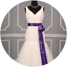 White lace wedding dress with a purple satin sash tied in a bow on a mannequin