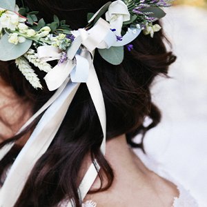 Woman's dark hair with a floral and ribbon crown, showing ribbons trailing down her back.